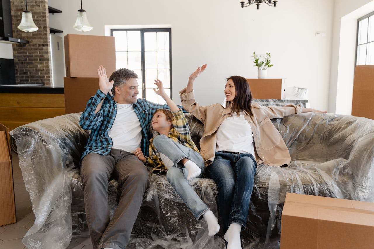 Home A cheerful family sitting on a couch amidst moving boxes, celebrating their new home.